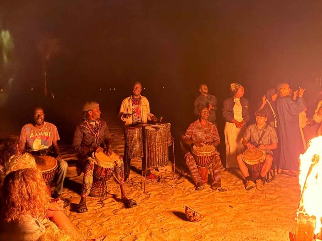 Students and local musicians performing djembe around a bonfire in Senegal
