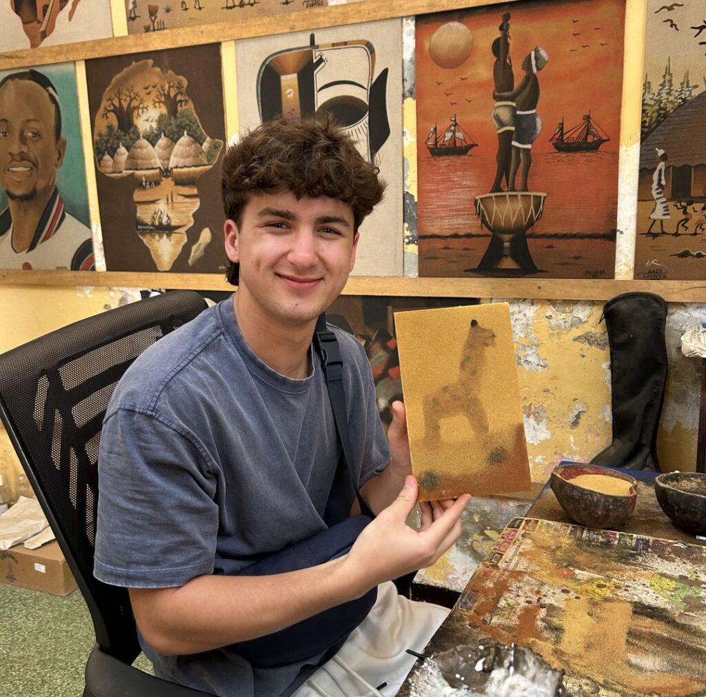 Student holding a handmade sand painting during an art workshop in Senegal